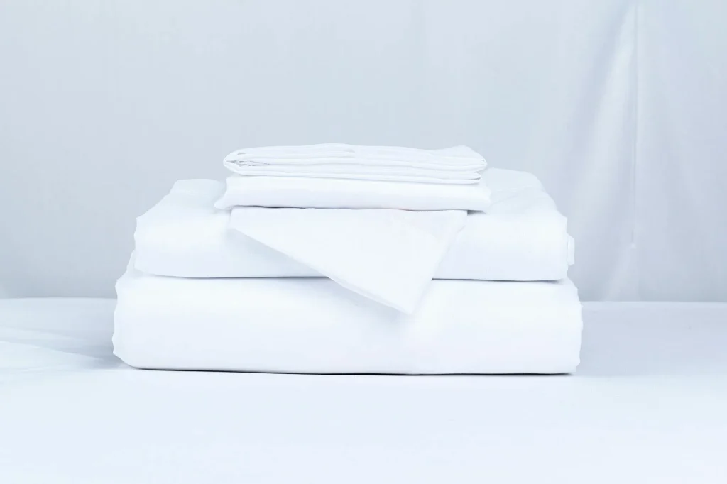 Crisp white cotton bed sheets on a neatly made bed in a bright bedroom