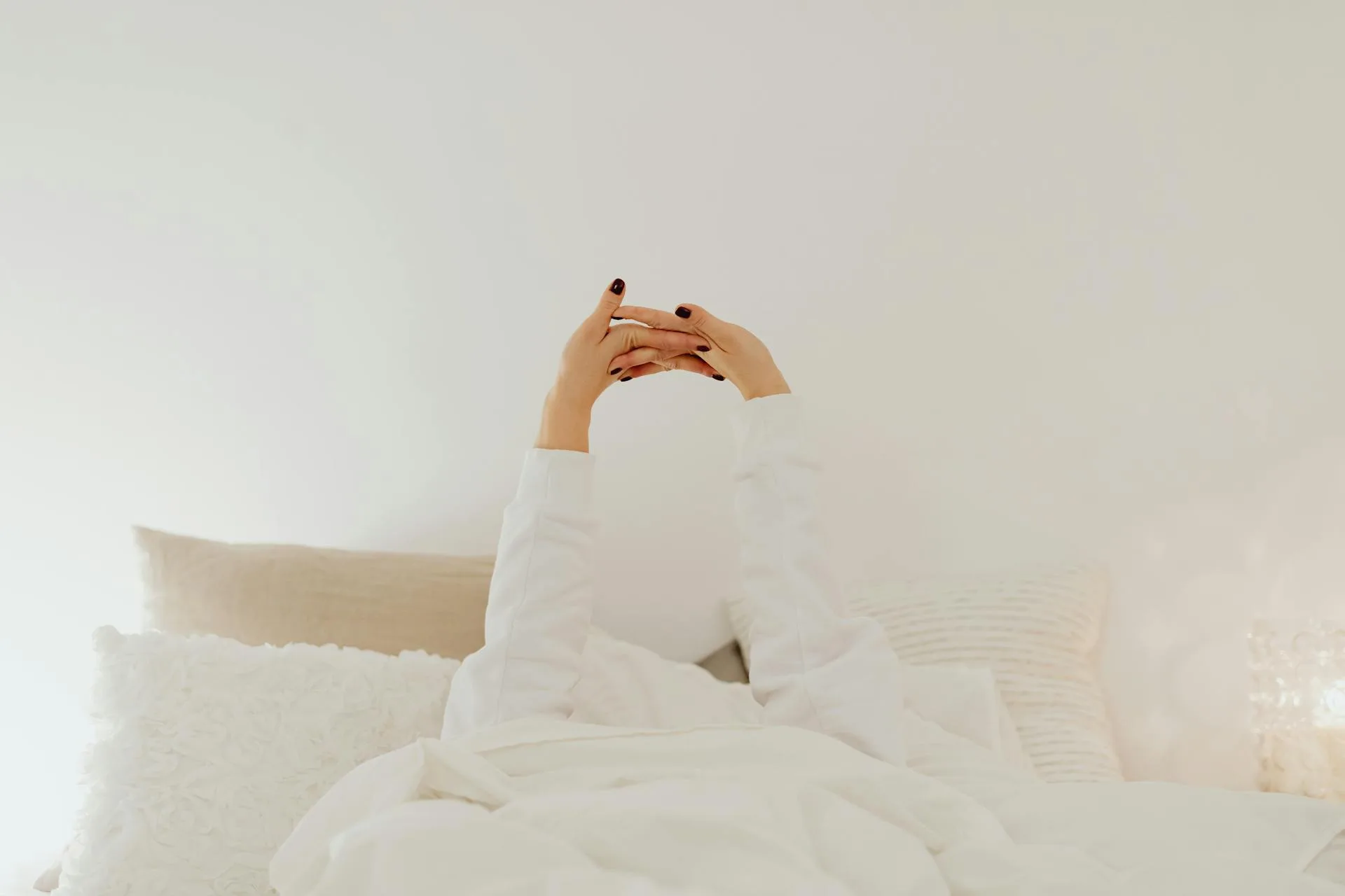 Cozy white duvet and pillows on bed with person stretching in morning
