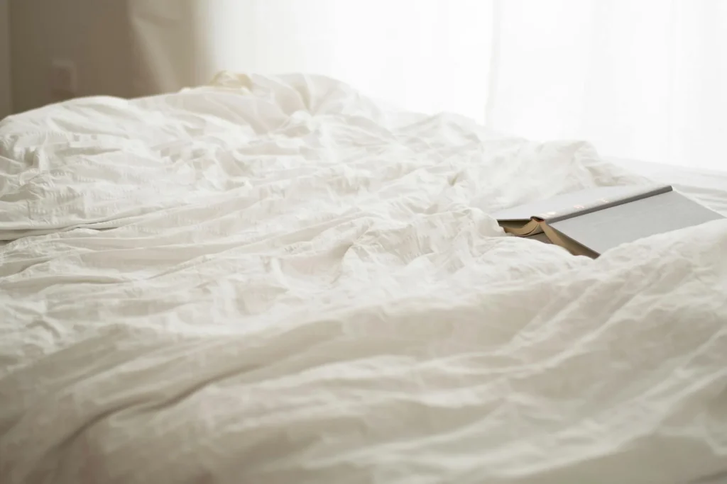Fresh white bed sheets in a bright bedroom with morning light and open book