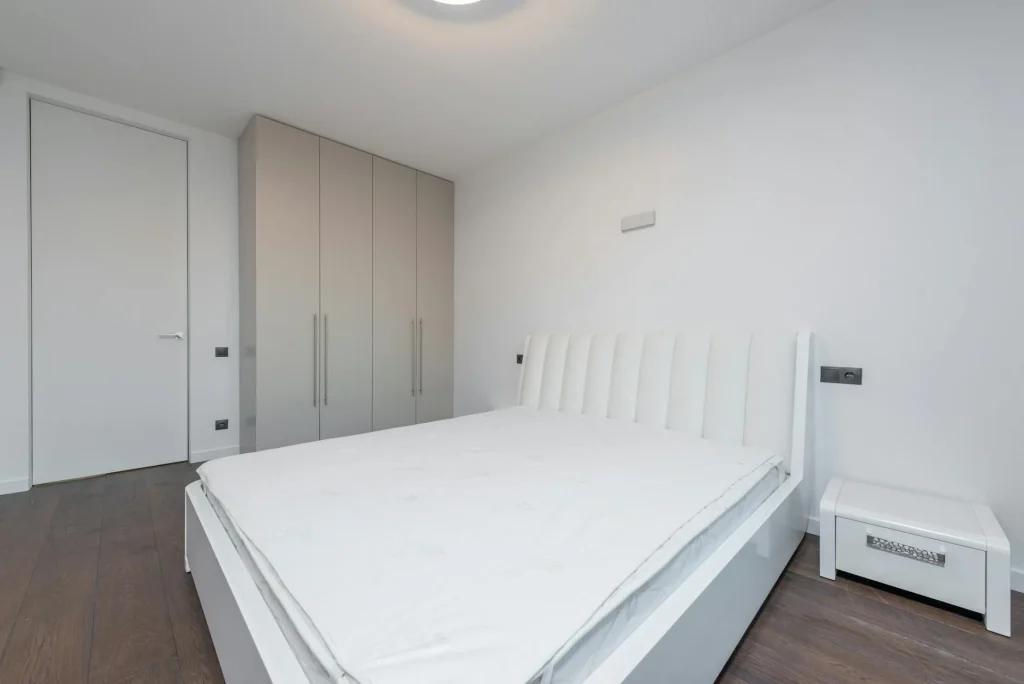 Clean white latex mattress on a bed frame in a bedroom