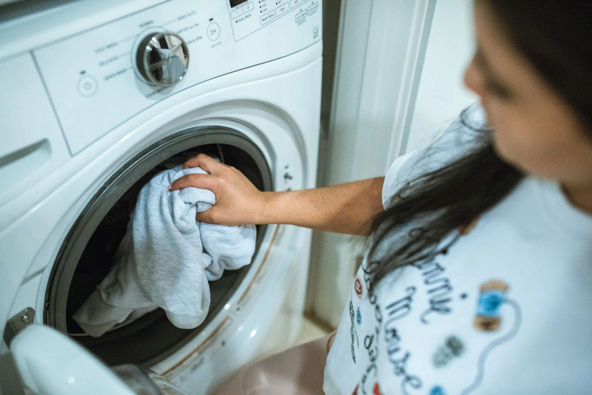 Person loading white bedding into a front-loading washing machine