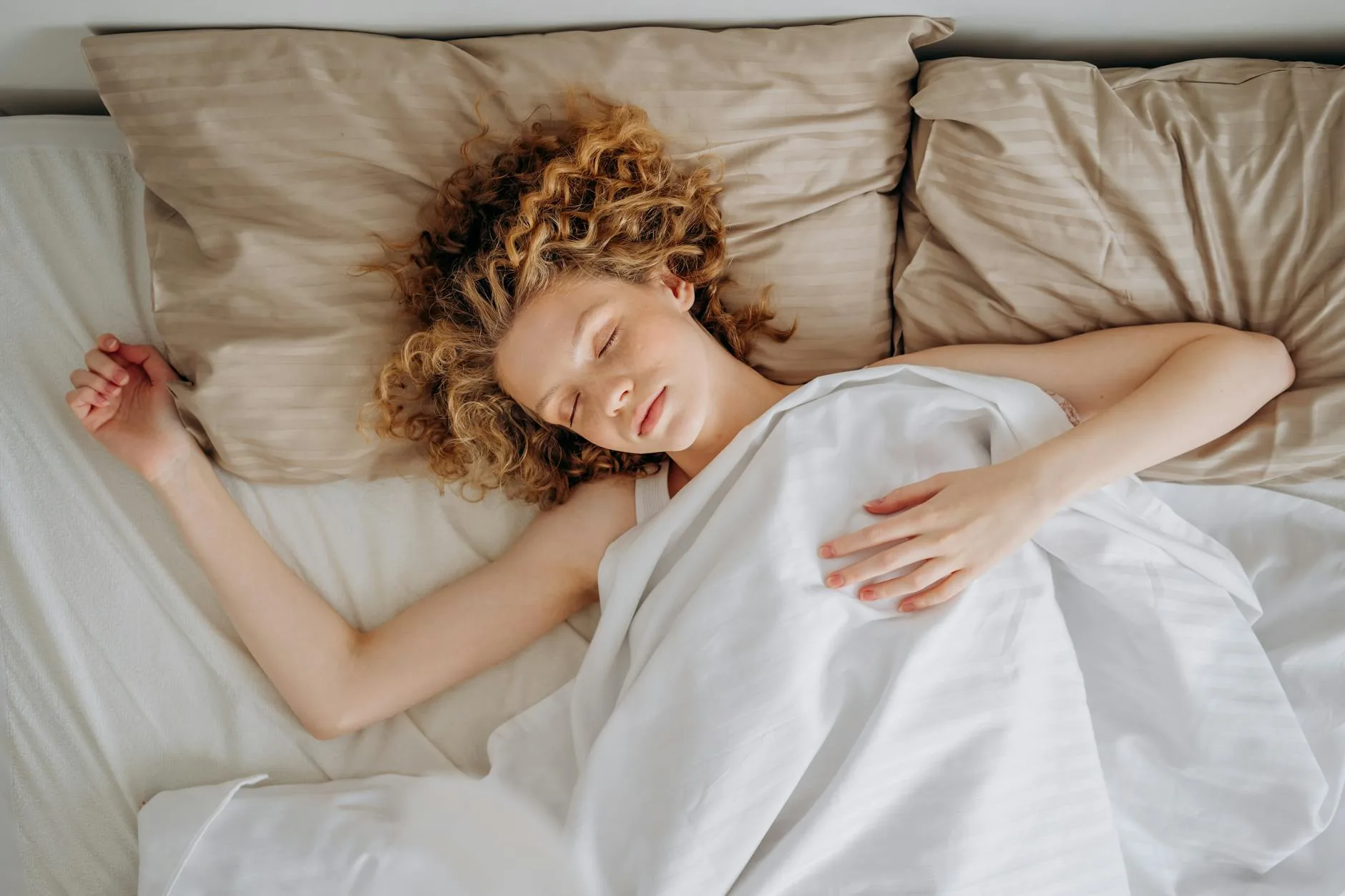 Woman sleeping peacefully under white bedding on mattress
