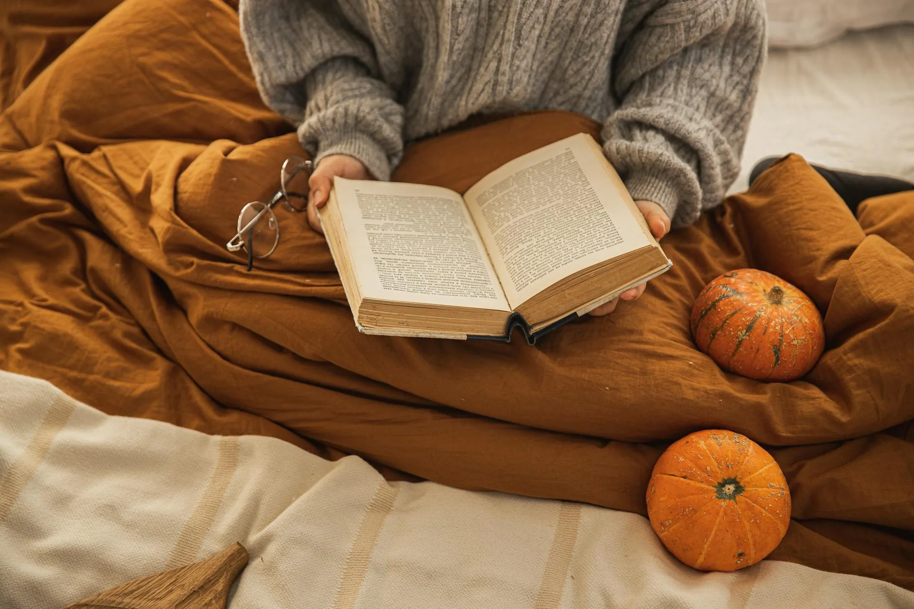 Person reading under a cosy blanket on a bed in the evening