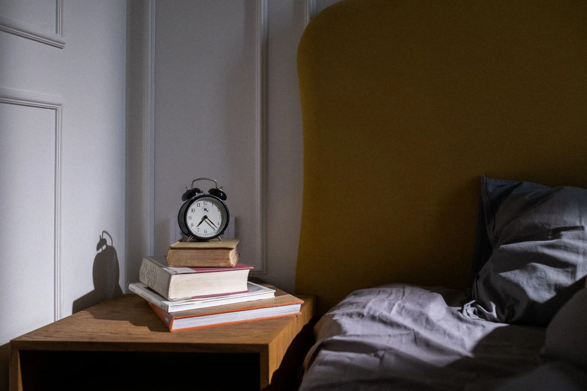 Bedside table with a book lamp and alarm clock instead of a phone